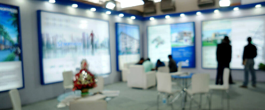 An out-of-focus picture of trade show attendees sitting down and reading posters.